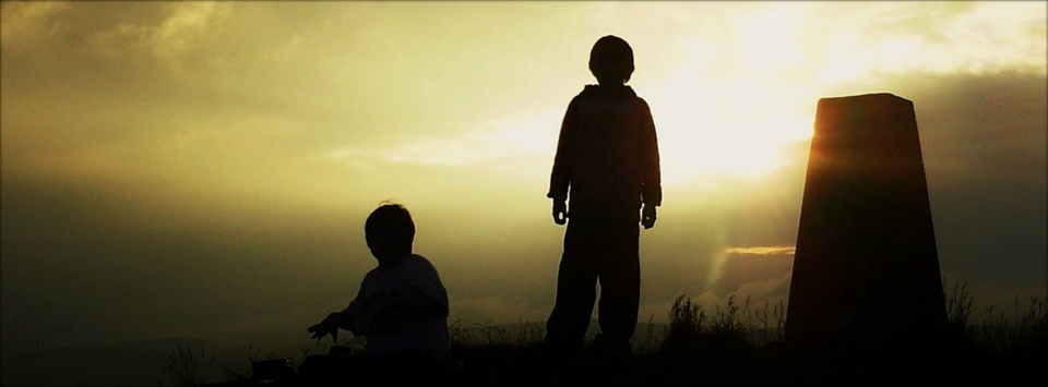 Children in silhouette by a trig point